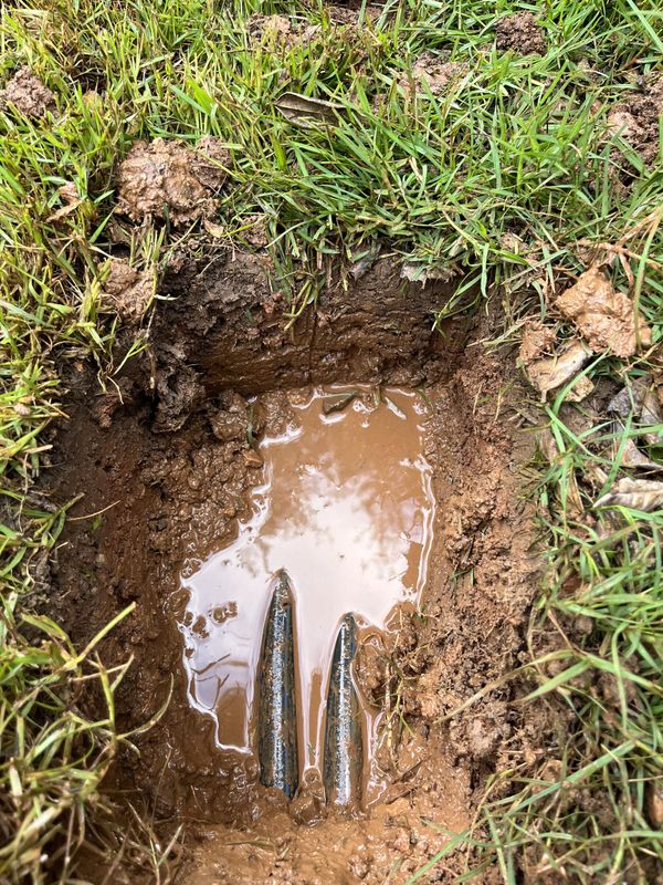 Un hoyo excavado en el césped que se llena de agua de una tubería principal de riego partida