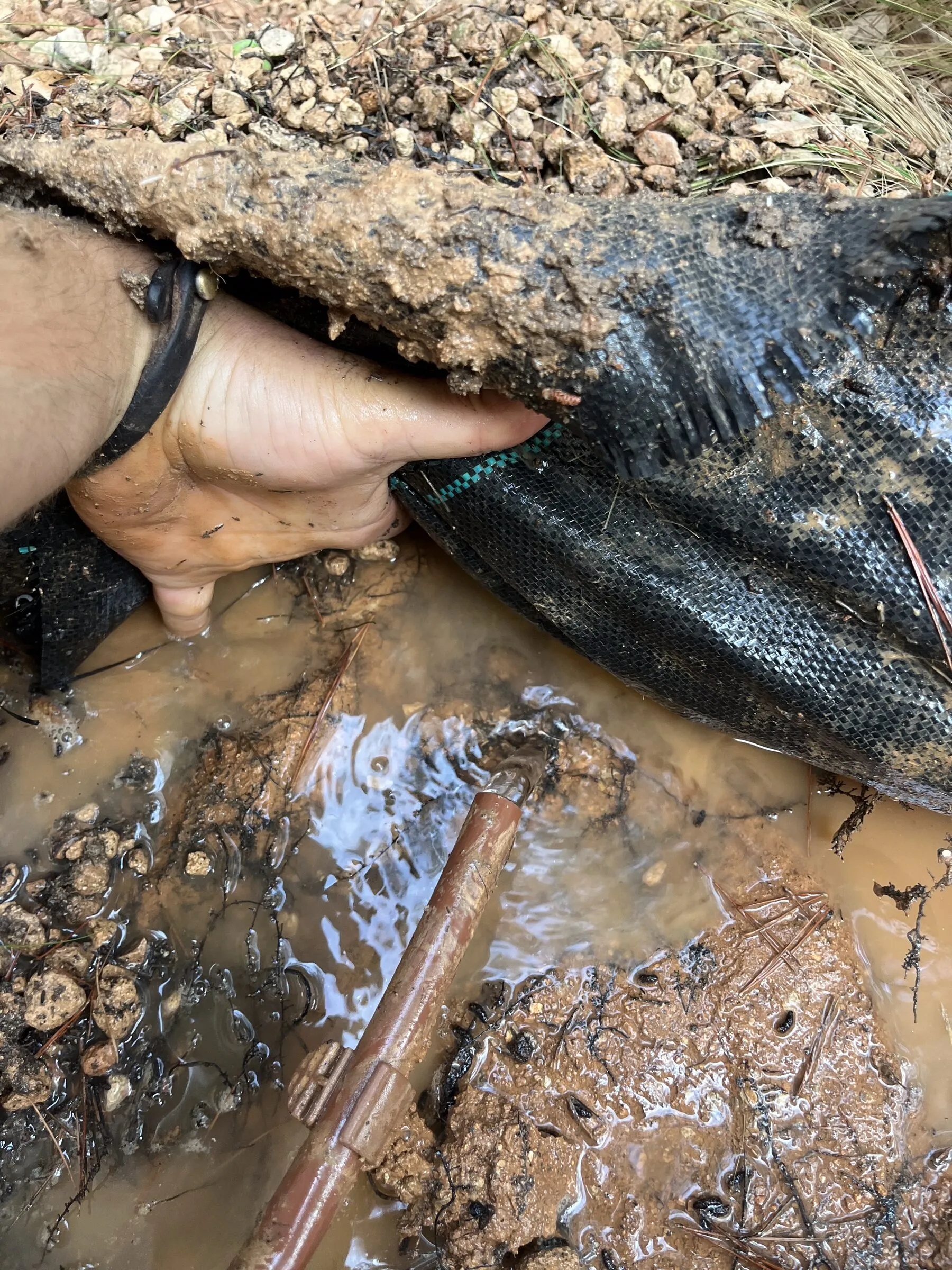 Water running beneath lifted geotextile membrane in a gravel bed
